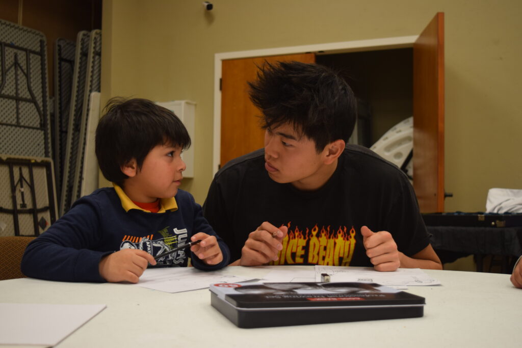 Young asian man volunteering to read with a Latino boy - elementary aged.